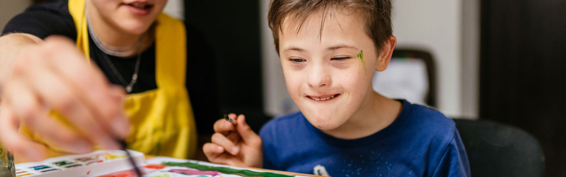 Ein Junge im Kindergartenalter mit einer Unterstützung beim Malen in einem Raum